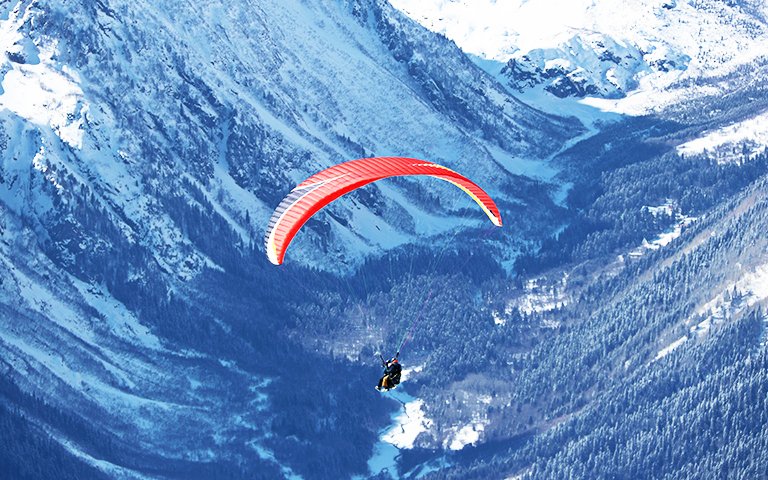 paraplane flying over snowy Caucasus mountains sunny blue sky